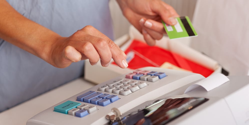 Midsection of saleswoman holding credit card while using ETR machine at boutique counter